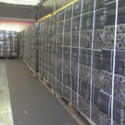 Równy rząd palet z kostkami opału drzewnego, zabezpieczonych folią i białym sznurkiem, wewnątrz naczepy pojazdu dostawczego.