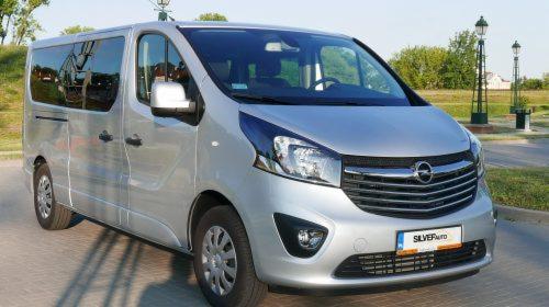 Srebrny Opel Vivaro z przesuwnymi drzwiami bocznymi, zaparkowany na zewnątrz w słoneczny dzień, z widoczną tablicą rejestracyjną SILVERAUTO.