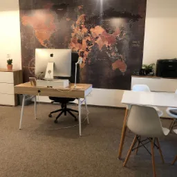 Biuro z biurkiem, komputerem Apple, krzesłem biurowym, stołem konferencyjnym i mapą świata na ścianie w tle.