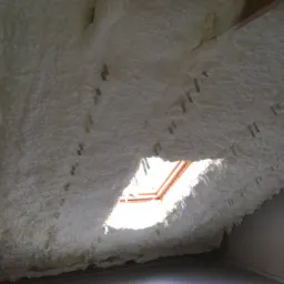 Poddasze po natrysku izolacji, widoczne metalowe uchwyty mocujące i fragment okna dachowego