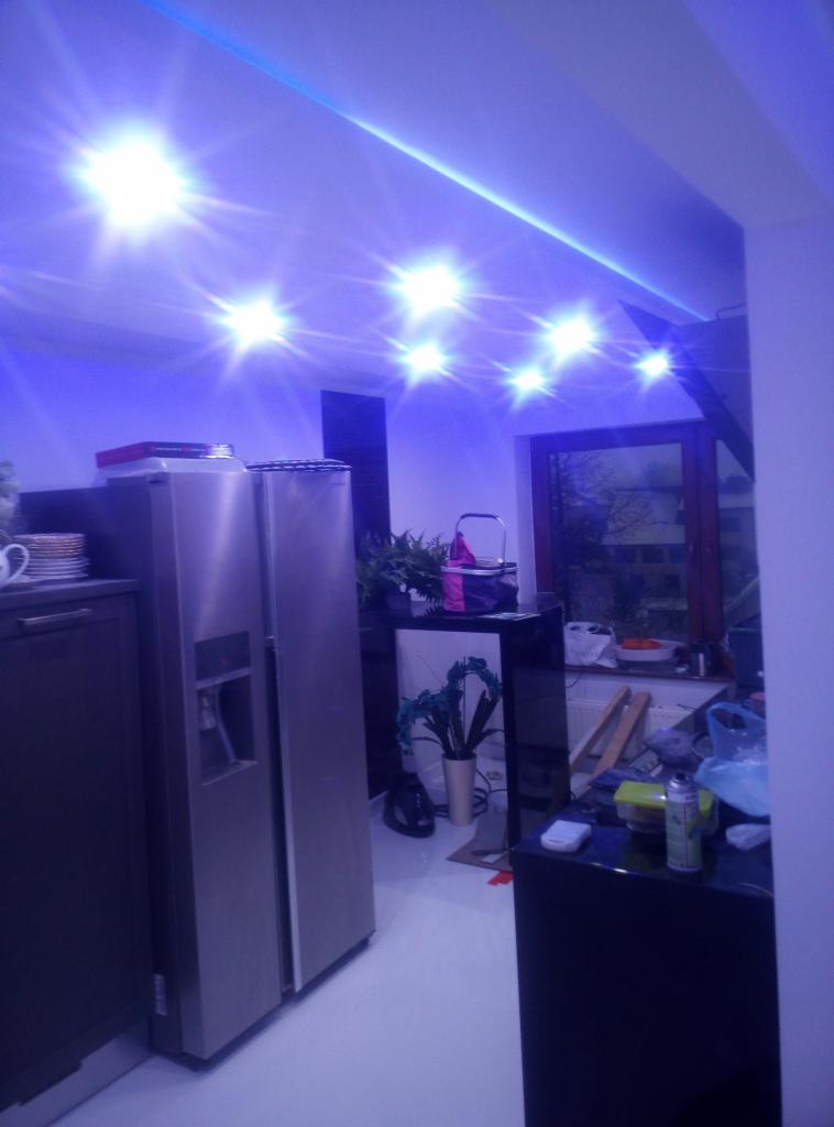 Kuchnia po remoncie z oświetleniem LED na suficie, widoczna zabudowa meblowa, lodówka side-by-side i okno z widokiem na zewnątrz.