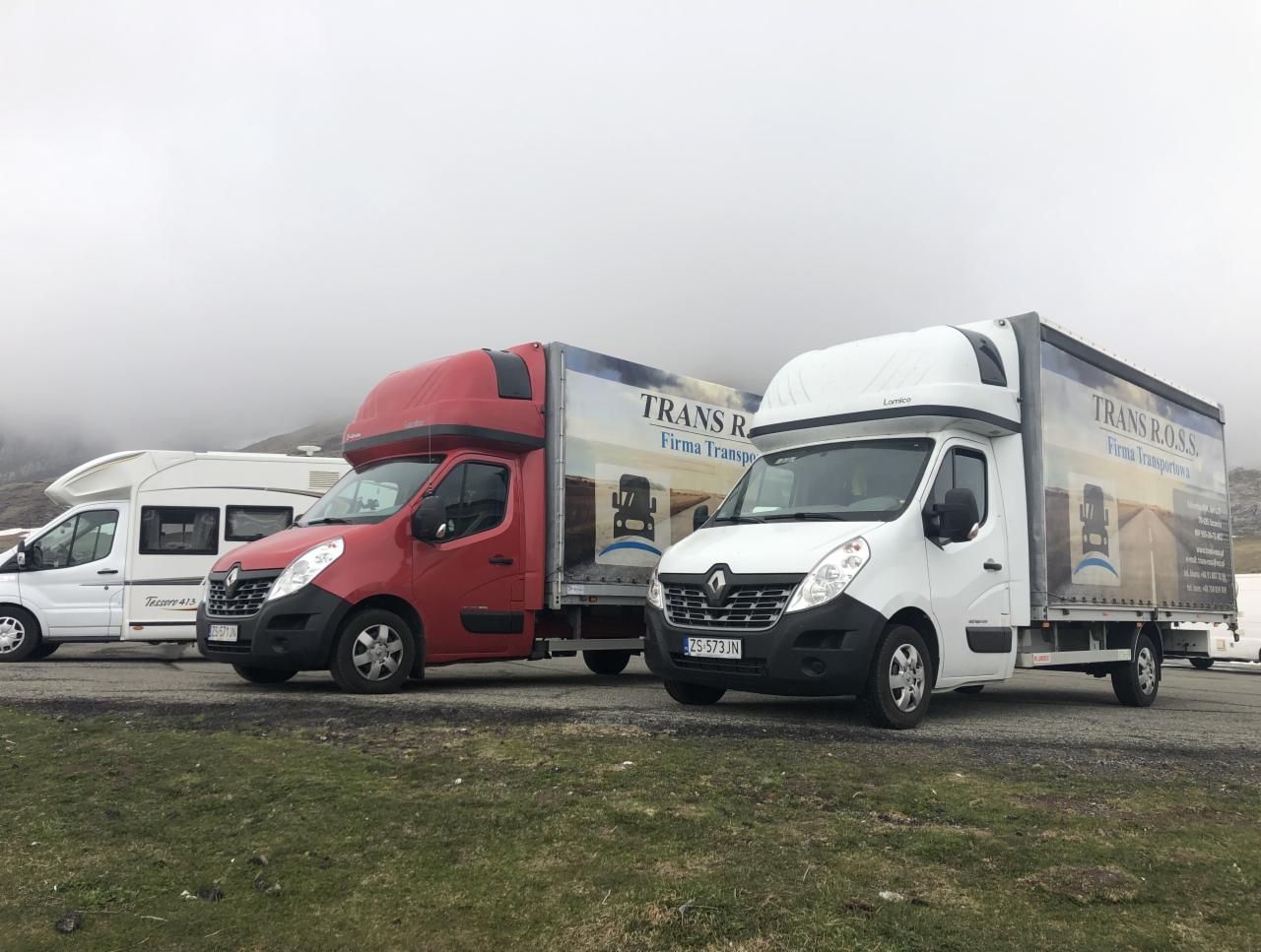 Trzy busy transportowe Renault Master z zabudową kontenerową i logo firmy TRANS R.O.S.S. zaparkowane na parkingu w górach, w tle mgła.