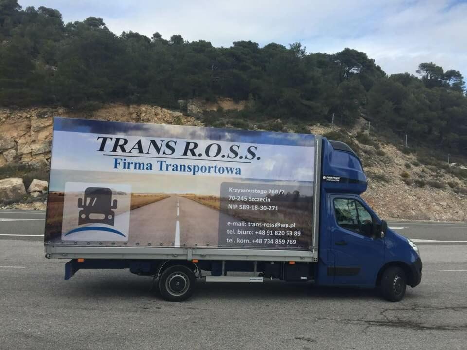 Niebieski bus dostawczy z reklamą firmy transportowej TRANS R.O.S.S. zaparkowany na poboczu drogi, z widocznymi danymi kontaktowymi i logo firmy na plandece.
