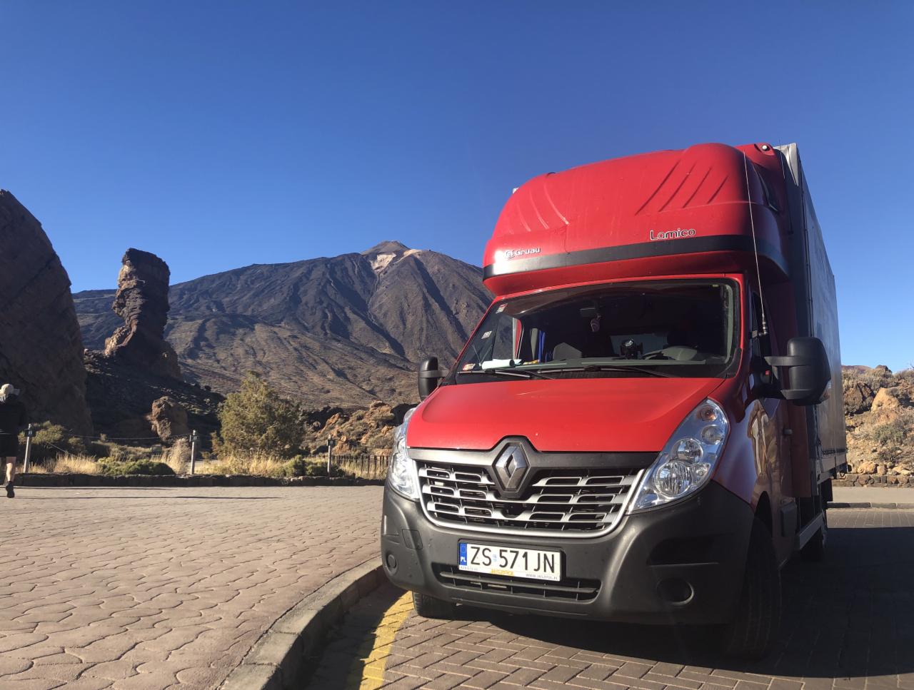 Czerwony bus Renault Master z nadbudową Lomico parkuje na tle krajobrazu wulkanicznego z widoczną górą Teide i formacją skalną Roque Cinchado.