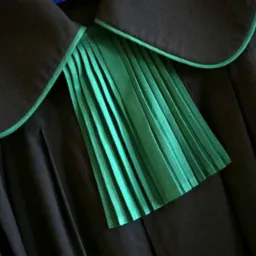 Detale togi prawniczej: czarny materiał z zielonymi plisami i obwódką kołnierza.