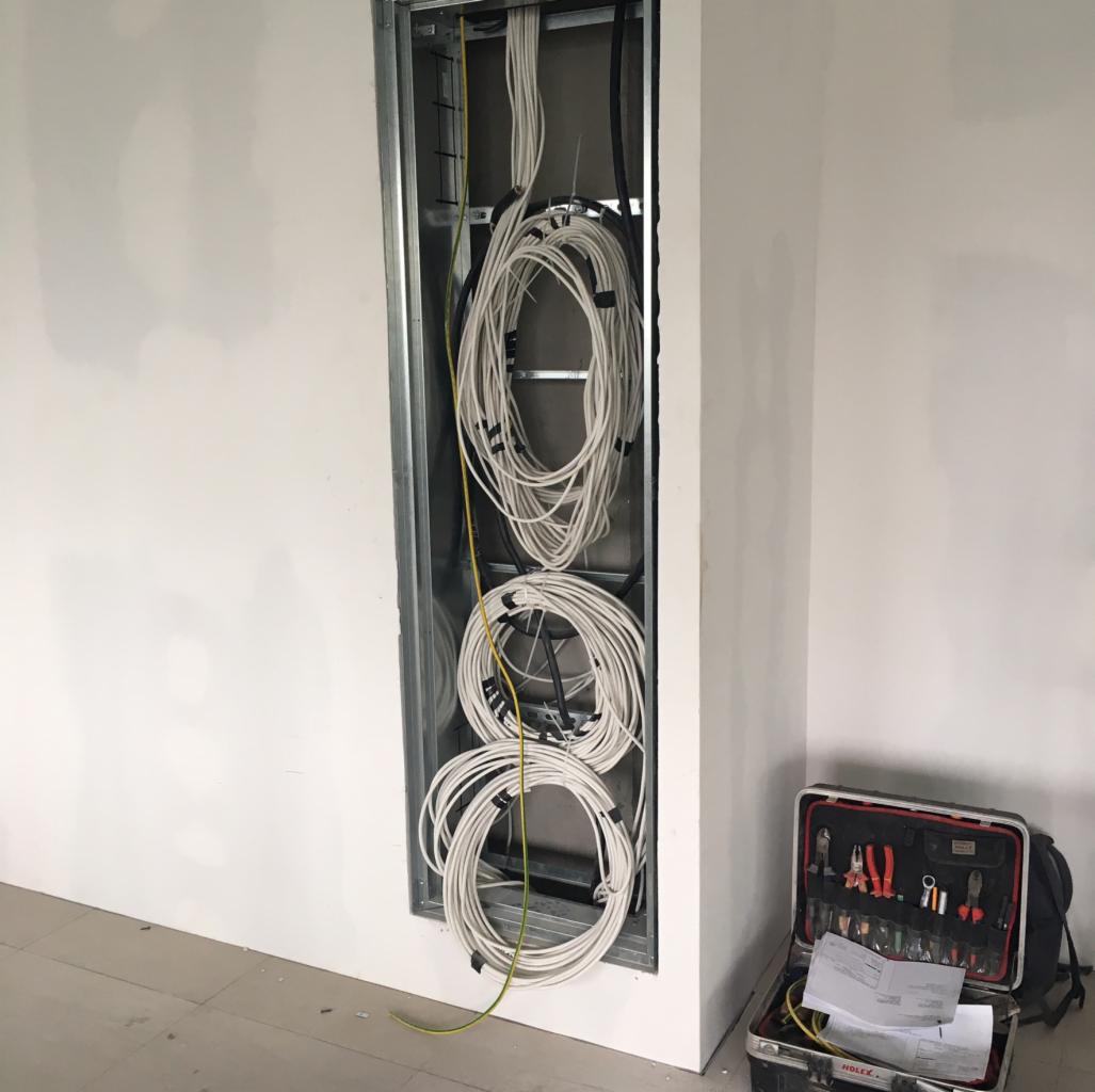 Wnęka w ścianie z ułożonymi kablami elektrycznymi zwiniętymi w okręgi, obok skrzynka z narzędziami.