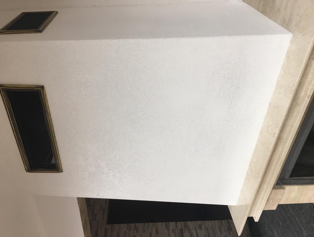 Biały sufit z dekoracyjną fakturą i dwoma prostokątnymi otworami wentylacyjnymi w złotych ramkach, widoczne wykończenie marmurowe.