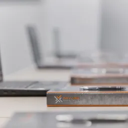 Sala szkoleniowa: laptopy i materiały z logo firmy szkoleniowej Orylion Szkolenia, długopis na materiałach.