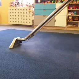 Profesjonalne czyszczenie wykładziny w pokoju dziecięcym za pomocą ekstraktora, widoczna para wodna podczas pracy urządzenia.