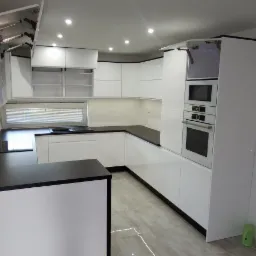 Nowoczesna, biała zabudowa kuchenna z czarnymi blatami, zrealizowana w Zamościu, z otwartymi górnymi szafkami i wbudowanym sprzętem AGD.