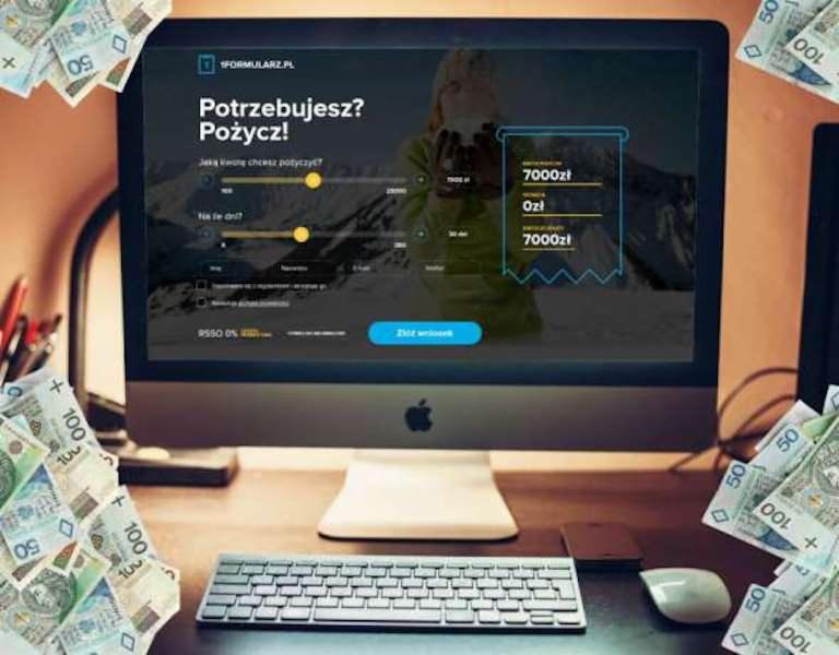 Ekran komputera z formularzem online do wnioskowania o pożyczkę, otoczony plikami banknotów o nominałach 50 i 100 zł, widoczne biurko z klawiaturą i myszką.