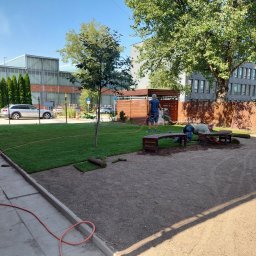 ARTI GARDEN - Układanie darni w rolkach na terenie zielonym w otoczeniu budynków biurowych, widoczne narzędzia i pracownicy podczas pracy.