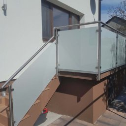 PEDROSTAL Mariusz Szyjka - Zewnętrzna balustrada ze szkła matowego i stali nierdzewnej, zamontowana przy schodach wejściowych do domu. Widoczne detale mocowania i satelita na elewacji.