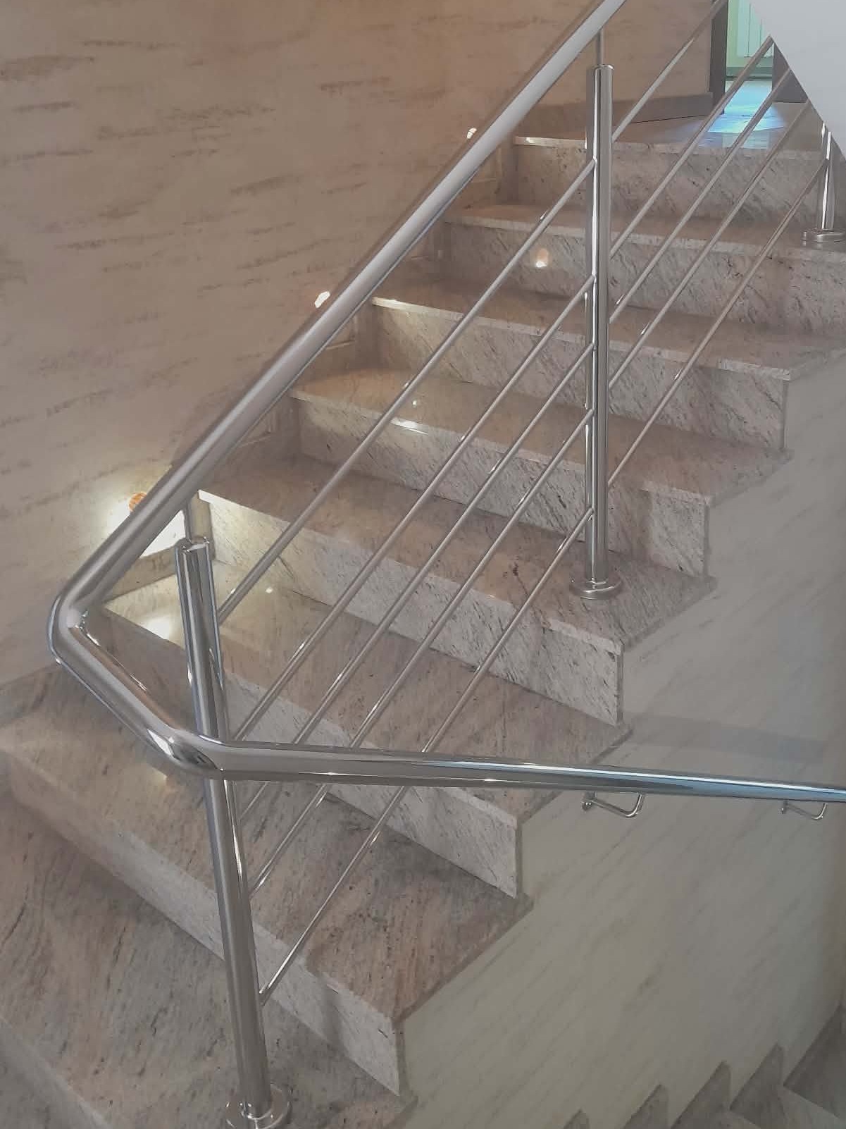 Polerowana balustrada ze stali nierdzewnej na marmurowych schodach. Minimalistyczny design, eleganckie wykończenie, widok z dołu.