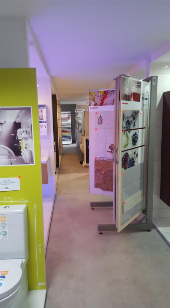 Wnętrze sklepu z wyposażeniem łazienek i podłóg, ekspozycja płytek ceramicznych i toalety na tle oświetlonego korytarza.