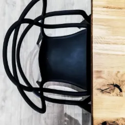 Czarny, designerski fotel z giętych rur obok drewnianego blatu stołu z widocznymi sękami, widok z góry.