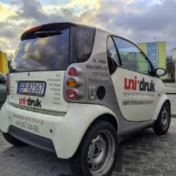 Smart z naklejkami reklamowymi drukarni Uni-druk, widoczne dane kontaktowe, tablica rejestracyjna i oferta: druk offsetowy i cyfrowy, ulotki, plakaty, wizytówki, banery, książki, naklejki.
