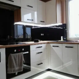 Nowoczesna kuchnia z białymi, lakierowanymi frontami, drewnianym blatem i czarnym panelem szklanym, oświetlona listwami LED pod szafkami wiszącymi i na podłodze, z czarną armaturą i piekarnikiem...