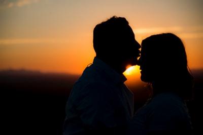 Silhouettes of a couple kissing at sunset, warm orange light highlighting their profiles.