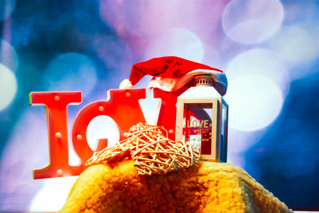 Kompozycja dekoracyjna z czerwonym napisem LOVE, wiklinowymi sercami, latarenką z napisem LOVE i czapką Mikołaja na rozmytym tle z bokeh.