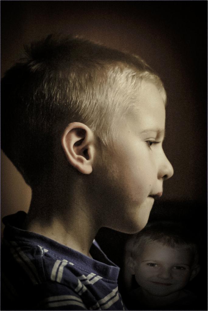 Portret profilowy chłopca z drugim, rozmytym chłopcem w tle, oświetlenie boczne podkreśla rysy twarzy.