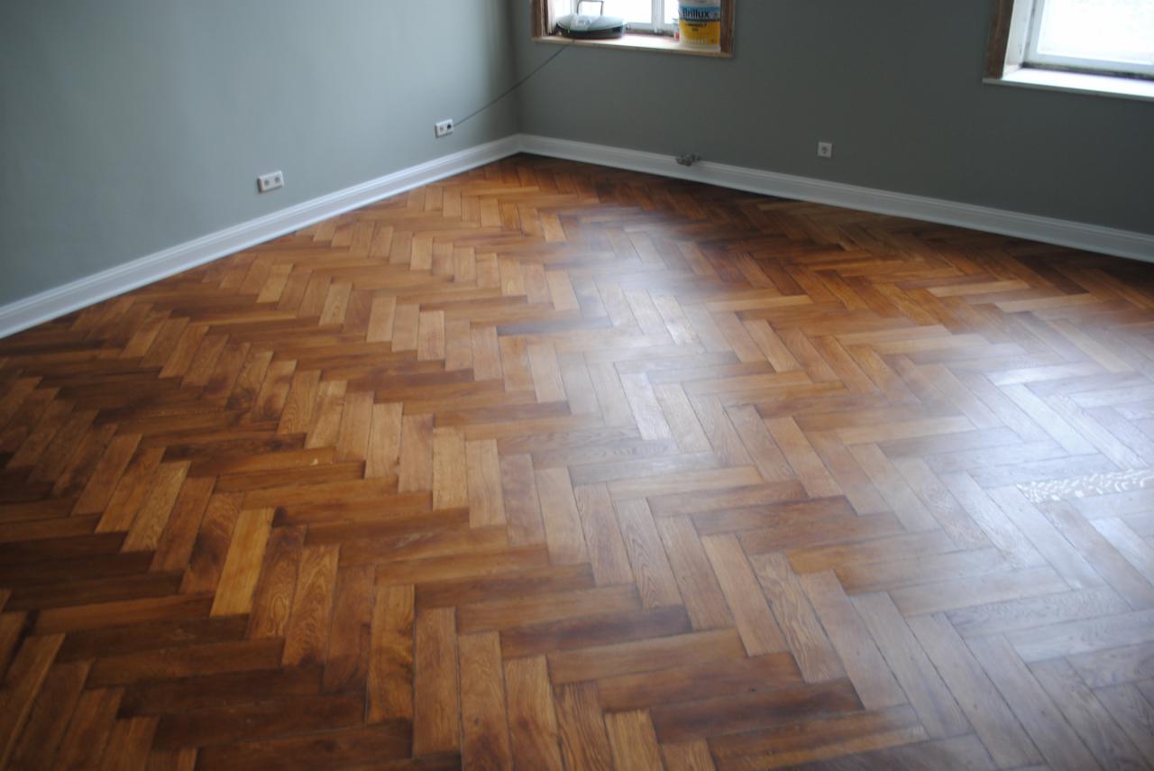 Parkiet ułożony w jodełkę po cyklinowaniu, widoczne ślady po procesie oraz puszka z lakierem na parapecie okna.