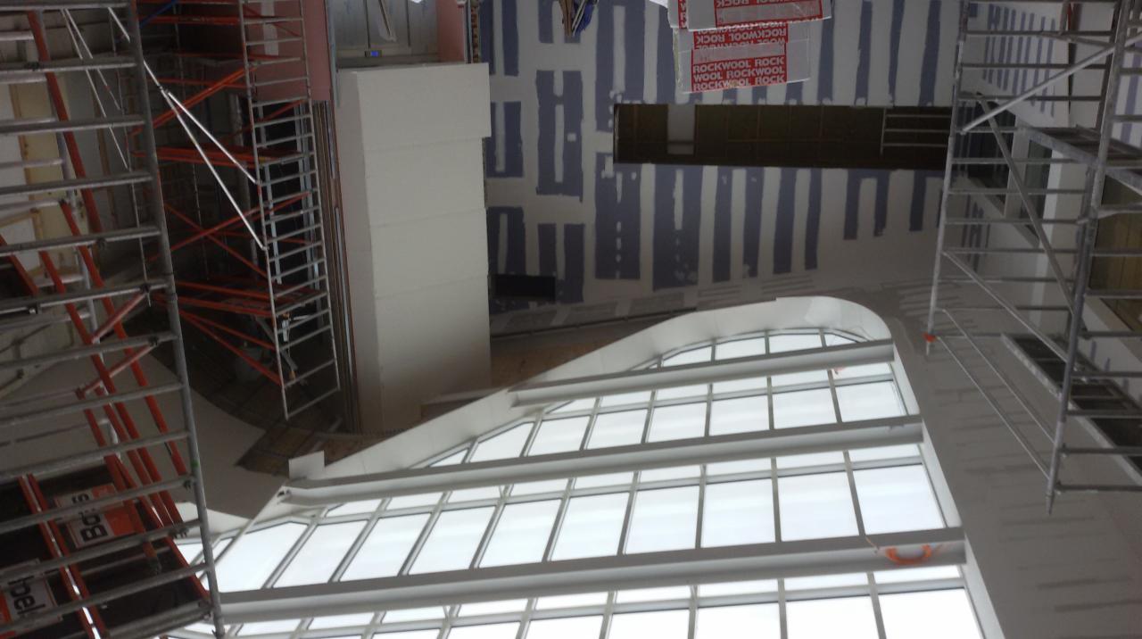 Wnętrze budynku w trakcie prac wykończeniowych, widoczne rusztowania, okna łukowe i ściany przygotowane do dalszych prac.