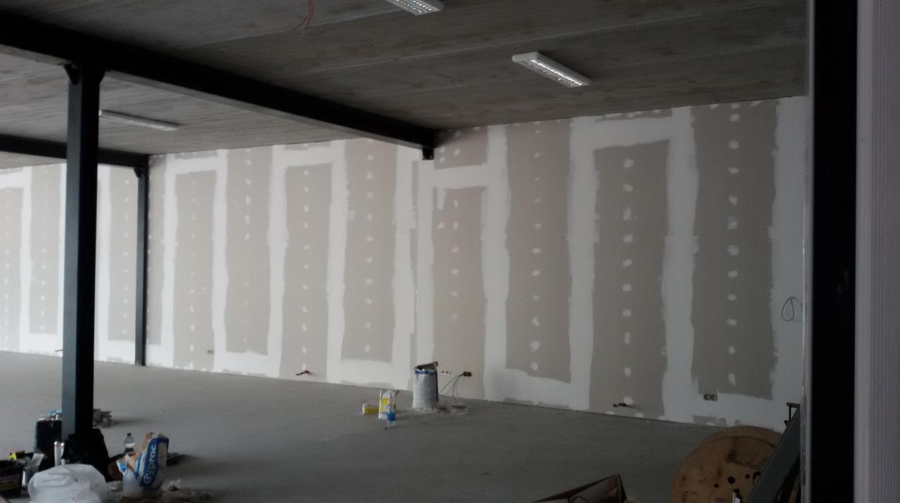 Montaż płyt kartonowo-gipsowych na ścianie w surowym stanie, widoczne metalowe profile, szpachlowane łączenia i wystające kable elektryczne.