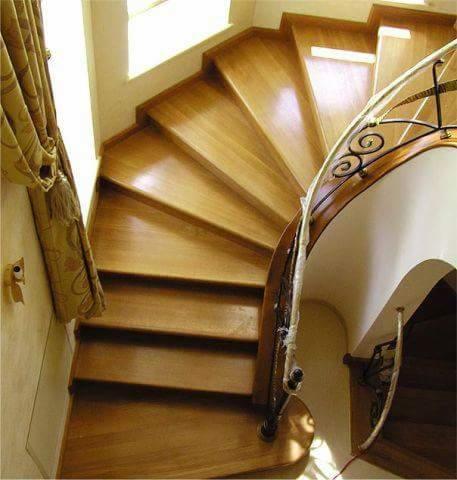 Widok z góry na spiralne schody z jasnego drewna z ozdobną, metalową balustradą i zasłoniętym oknem po lewej stronie.