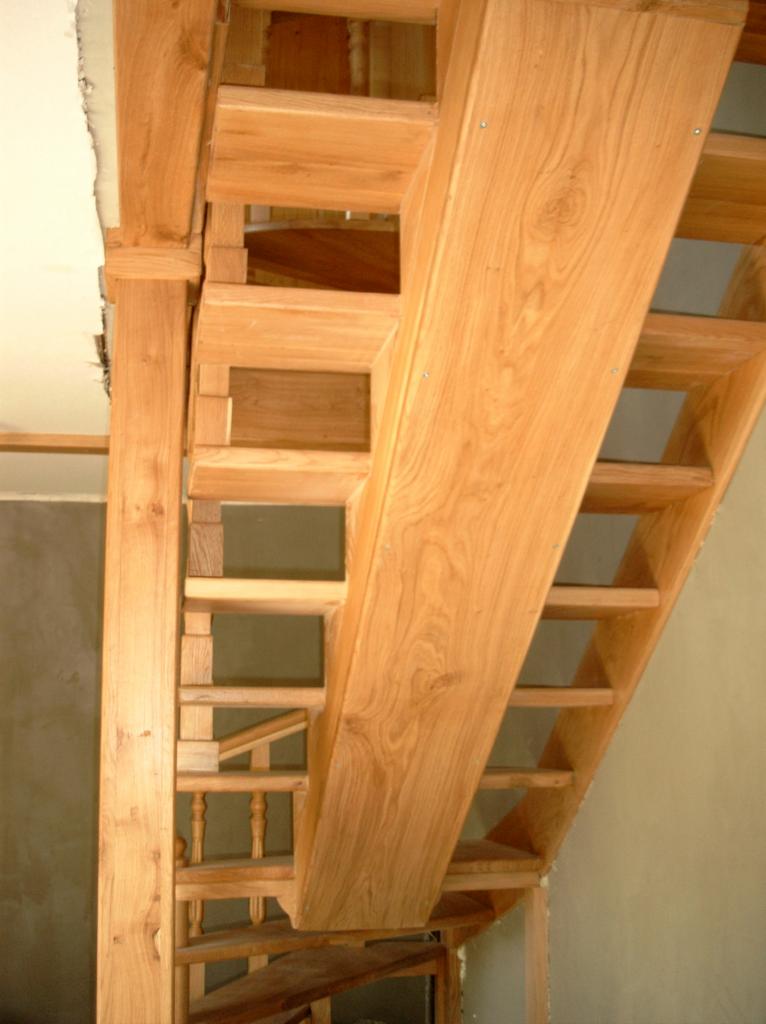 Surowe, jasne drewniane schody w trakcie montażu; widoczne niedoskonałości ścian i sufitu, podkreślające etap budowy.