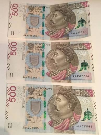 Trzy banknoty 500 zł ułożone jeden pod drugim, widoczne numery seryjne AA4325083, AA4325084 i AA4325085. Banknoty leżą na jasnej powierzchni.