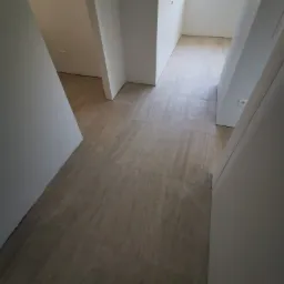 Korytarz po remoncie z beżową podłogą imitującą kamień i białymi ścianami z widocznymi gniazdkami elektrycznymi.