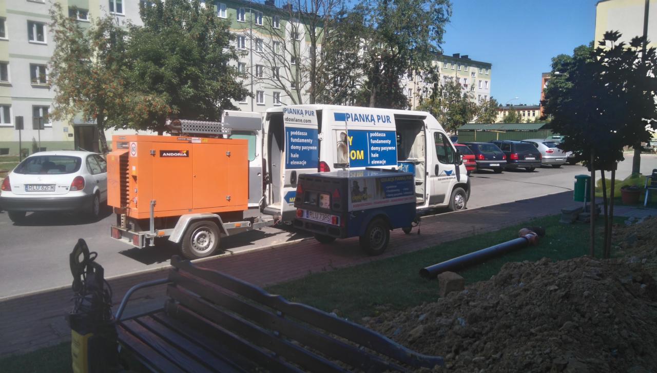 Mobilny zestaw do ocieplania pianką PUR na parkingu, z widocznym agregatem prądotwórczym Andoria, przyczepką i samochodem dostawczym z reklamą firmy.