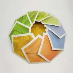 Okrąg z kartoników w kształcie wielokątów z motywami liści w różnych kolorach (zielony, żółty, pomarańczowy, niebieski), tworzących graficzną kompozycję na białym tle.