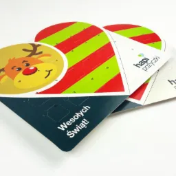 Trzy kalendarze adwentowe w kształcie serca i trójkąta, z reniferem, paskami i logo firmy, na białym tle.