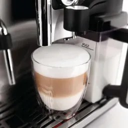 Automatyczny ekspres do kawy w trakcie przygotowywania latte macchiato w szklance z podwójnymi ściankami; widoczny pojemnik na mleko z oznaczeniem MAX.