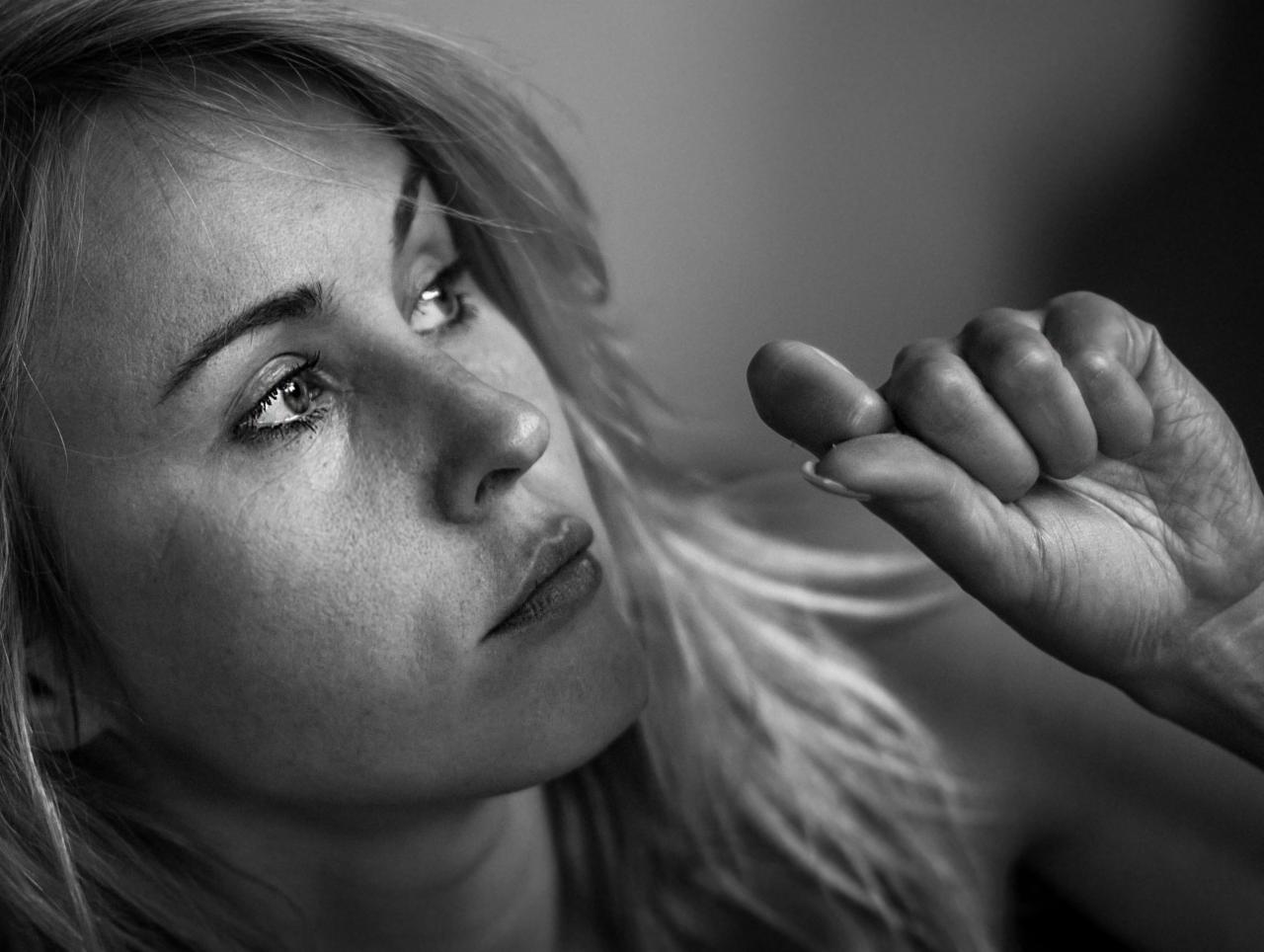 Portret kobiety z lekko zmarszczonym czołem, spoglądającej w górę, z dłonią w kadrze, czarno-białe zdjęcie.