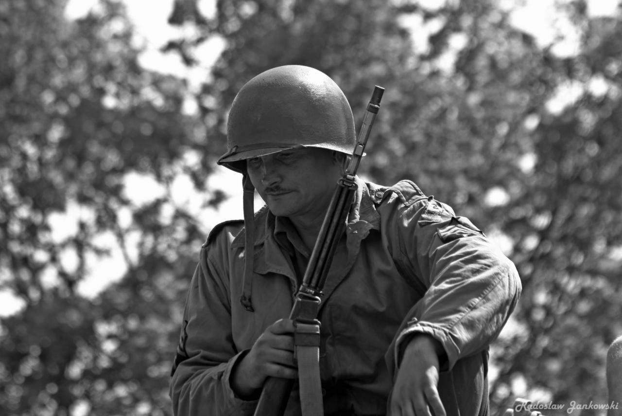 Czarno-białe zdjęcie mężczyzny w hełmie i mundurze, trzymającego karabin, prawdopodobnie rekonstrukcja historyczna.
