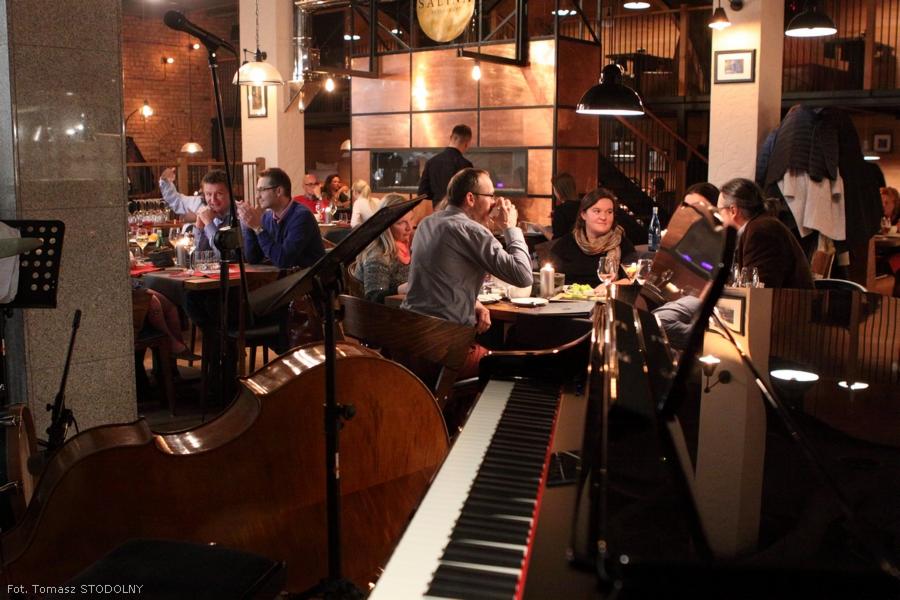 Wnętrze restauracji Salina w Bochni podczas wieczoru z muzyką na żywo: goście siedzą przy stolikach, w tle widoczny kontrabas i fortepian.