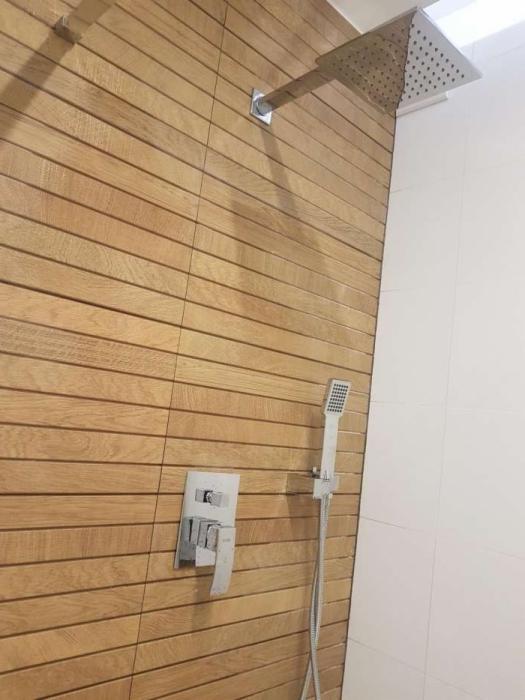 Nowoczesna kabina prysznicowa z drewnopodobnymi płytkami ułożonymi poziomo, deszczownicą i baterią podtynkową.