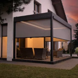 Zadaszony taras z meblami ogrodowymi i roletami pionowymi, oświetlony od wewnątrz, na tle zachodzącego słońca.