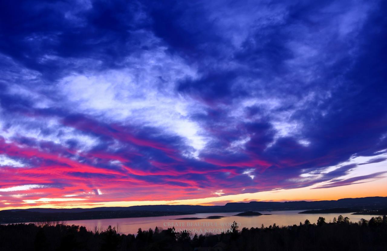 Rozległy widok na jezioro o zmierzchu, z intensywnie niebieskim niebem poprzecinanym pasmami różowych i pomarańczowych chmur, ciemny pas lasu w dolnej części kadru.