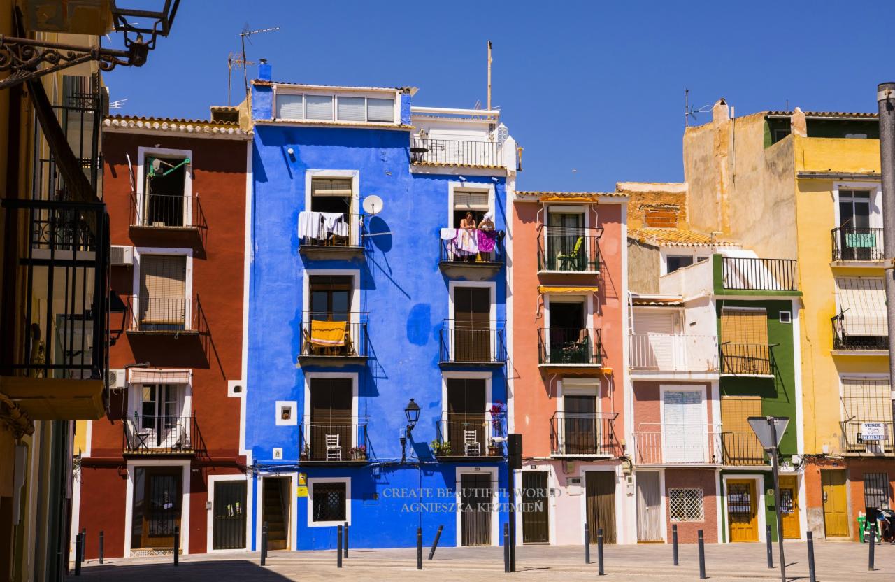 Colourful facades of Mediterranean buildings with balconies, laundry hanging on the blue building's balcony, clear blue sky.