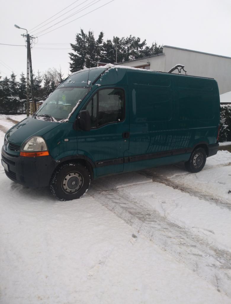 Zielony samochód dostawczy Renault Master zaparkowany na śniegu przed budynkiem w pochmurny dzień.