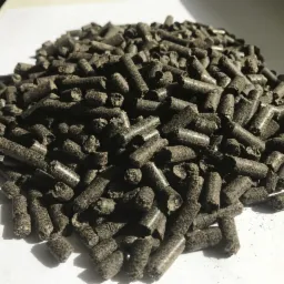 Kupa ciemnych peletów na jasnym tle, oferowanych w Pysznicy. Widoczne nieregularne kształty i struktura powierzchni peletów. Lekkie cienie podkreślają trójwymiarowość.