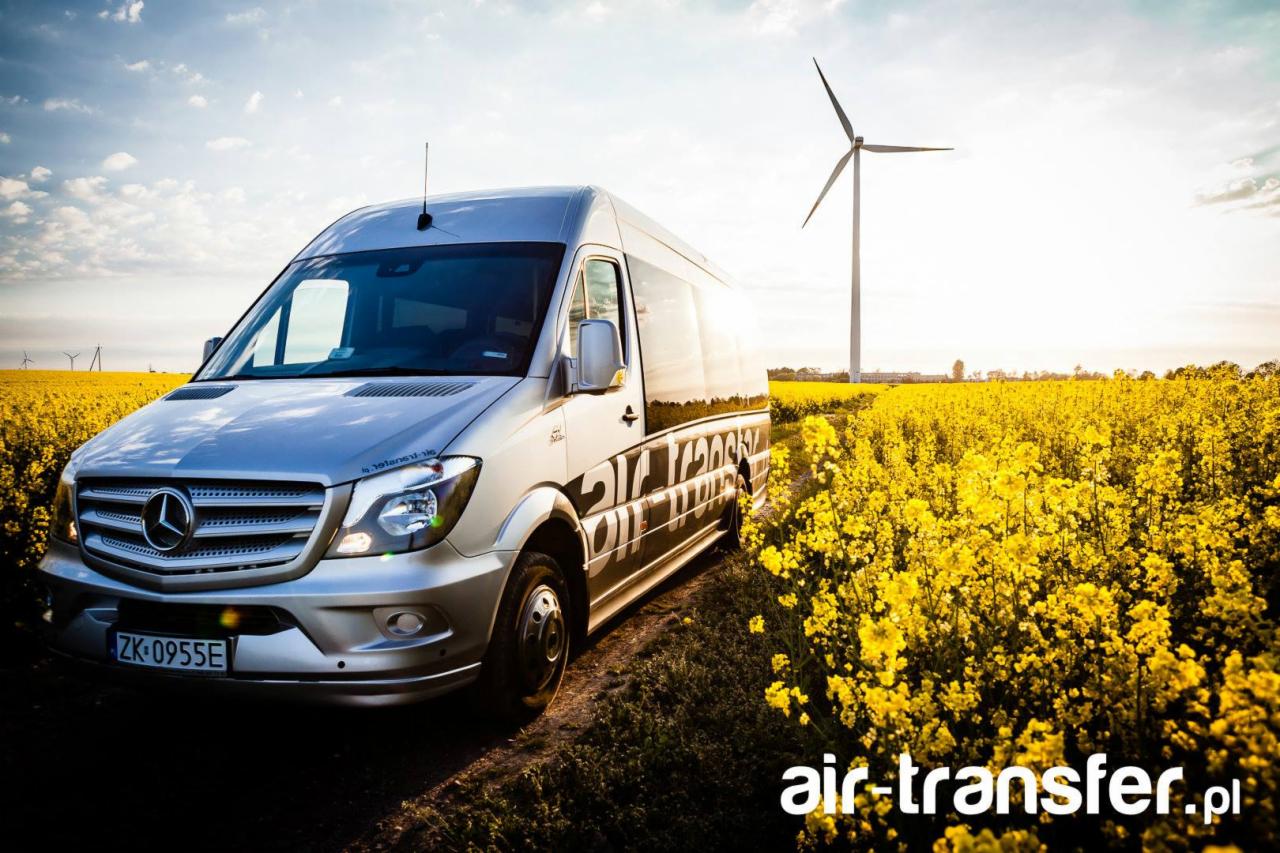 Srebrny bus Mercedes z napisem 'air-transfer.pl' na tle pola kwitnącego rzepaku i turbiny wiatrowej.