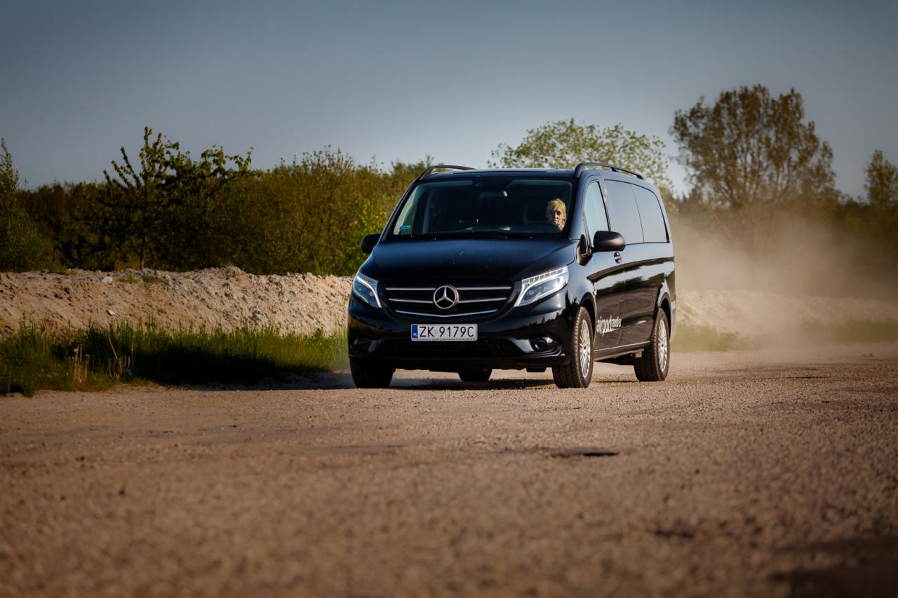 Czarny Mercedes Vito z kierowcą na polnej drodze, tablica rejestracyjna ZK 9179C, logo firmy airporttransfer widoczne na boku.
