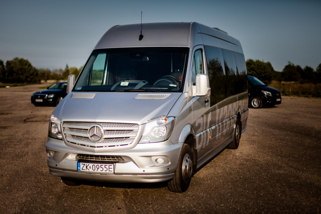 Srebrny bus Mercedes-Benz z polską tablicą rejestracyjną ZK 0955E na parkingu, z dwoma czarnymi samochodami w tle.
