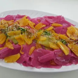 Świąteczna sałatka z marynowanych buraków, pomarańczy i kiełków na białym talerzu w kształcie liścia.