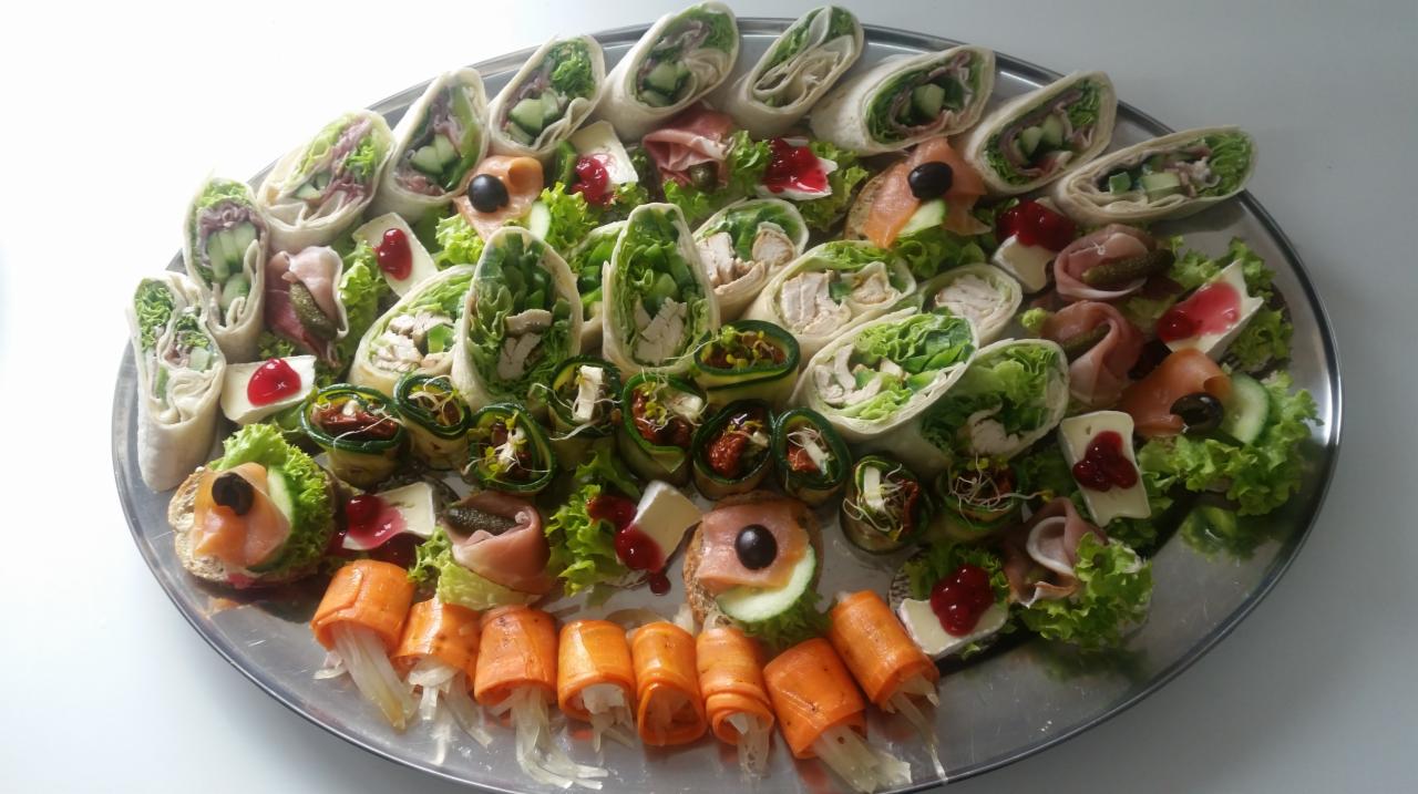 Srebrna patera z różnorodnymi przekąskami: tortille z warzywami i mięsem, roladki z cukinii, kanapeczki z łososiem i serem brie z żurawiną, dekorowane sałatą i oliwkami.